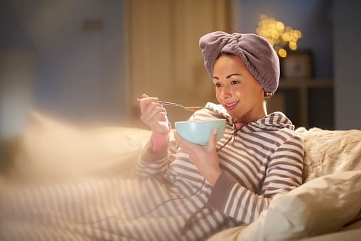 young woman enjoying healthy soup for dinner while watching TV